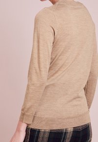 Beżowy sweter z prążkowanym dekoltem i mankietami, posiadający długie rękawy i luźny krój, w połączeniu z wzorzystą spódnicą.