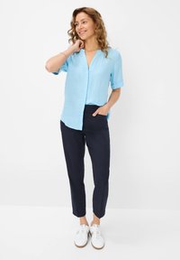Lichtblauw linnen overhemd met korte opgerolde mouwen en een V-hals, gecombineerd met aangesloten marineblauwe broek en witte sneakers.