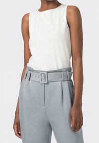 Vit ärmlös topp med rund halsringning, tillsammans med ljusgrå högmidjade byxor med bälte och sidofållar.