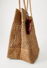 Geflochtene Strohtasche in einem natürlichen Tan-Farbton mit einer strukturierten Oberfläche. Sie verfügt über zwei robuste Henkel und eine farbenfrohe Quaste als Verzierung.