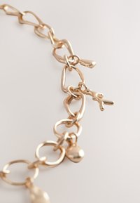 Gold-toned chain with varying link shapes, including round and oval, featuring small charms and a smooth, polished texture.