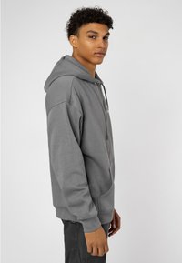 Gray zip-up hoodie with a front pocket, soft texture, and drawstring. Features ribbed cuffs and hem, plain design without patterns.