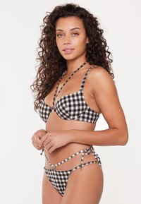 Bikini à carreaux noir et blanc avec un soutien-gorge à armatures, détails de fines bretelles et liens sur les côtés du bas. Tissu lisse avec un design structuré.