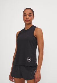 Top atlético negro sin mangas con escote redondeado y dobladillo con aberturas laterales. Presenta un logo en la parte inferior frontal. Combinado con pantalones cortos negros a juego.