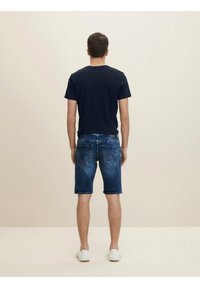 Navy blue t-shirt paired with blue denim shorts featuring a faded wash and back pockets. Worn with white sneakers. Simple design.