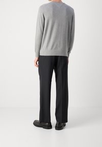 Grijze gebreide trui met lange mouwen en een ronde hals, gecombineerd met zwarte, op maat gemaakte broek en zwarte schoenen, gezien van achteren.