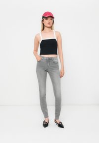 Crni skraćeni top s bijelim trakama, sivi skinny traperice i crne cipele na špic. Crvena kapa s crnim detaljima upotpunjuje odjevnu kombinaciju.