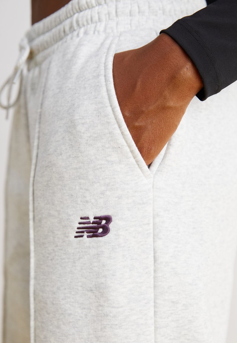 Lichtgrijze katoenen joggers met een elastische tailleband, zijzakken en een paarse geborduurde New Balance-logo op de dij.