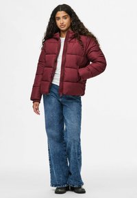 Burgundy puffjacka med dragkedja fram, med hög krage och horisontellt quiltat mönster. Kombinerad med vida blå jeans.