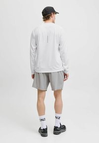 Witte langemouwen shirt met een grijze verticale streep op de rug, gecombineerd met grijze shorts en zwarte sneakers. Accessoires zijn een zwarte pet.