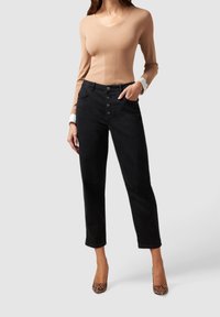 Top de manga larga acanalado color marrón claro combinado con jeans negros de tiro alto que cuentan con un cierre frontal de botones y tacones con estampado de serpiente texturizado.