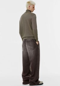 Olivgrüner, figurbetonter Pullover mit hohem Kragen und langen Ärmeln, kombiniert mit weiten braunen Cordhosen, die zwei hintenliegende Taschen haben.