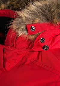 Rød vinterjakke med hætte foret med pels, med trykknapper og syninger. Stoffet ser tekstureret og vandafvisende ud.