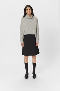 Un pull léger gris clair avec col cheminée associé à une jupe noire de longueur genou. Présente des chaussettes noires à motifs et des ballerines noires à talons pointus. Design simple et moderne.