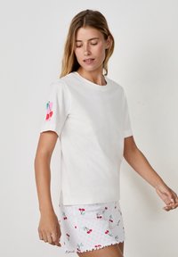 Biała bawełniana koszulka z krótkim rękawem, z kolorowym wzorem wiśni na lewym rękawie. Gładka tekstura, okrągły dekolt.