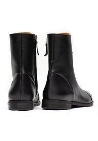Stivali alla caviglia in pelle nera con una texture liscia, cuciture sottili e design slip-on. Presentano una zip laterale e un tacco basso e piatto.