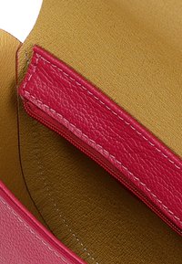 Interno di una borsa in pelle con una fodera dorata testurizzata, una tasca con zip rossa e dettagli di cucitura a contrasto. Finitura liscia e resistente.