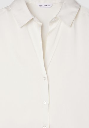 Blusa bianca leggera con colletto, chiusura frontale a bottoni e una consistenza liscia simile alla seta. L'etichetta del marchio è visibile.