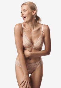 Zestaw koronkowej bielizny w delikatnym odcieniu brzoskwiniowym, z falbaniastymi krawędziami i kwiatowymi wzorami. Biustonosz ma regulowane ramiączka, a majtki mają pasujący wzór.