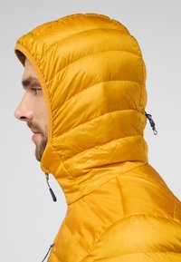 Veste isolante jaune avec une capuche, présentant un design matelassé, une texture lisse et des détails de fermeture éclair sur les côtés.