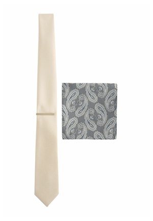 Cravate solide crème de largeur fine avec une finition texturée, accompagnée d'un pochette de costume gris à motif paisley avec des motifs blancs complexes.