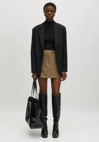Schwarzer oversized Blazer, gerippter schwarzer Rollkragenpullover, beiger Minirock, knielange schwarze Stiefel und glänzende schwarze Handtasche. Sanfte Texturen und neutrale Farben.