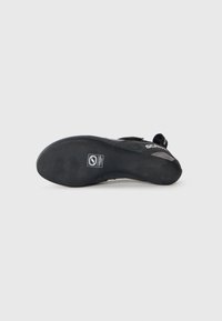 Black climbing shoe featuring a textured rubber sole, sleek design, and velcro strap for a secure fit. Brand logo visible on the sole.