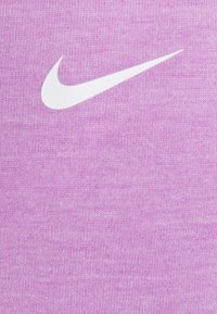Jasnofioletowa koszula z materiału, na której widnieje biały logo Nike w kształcie łyżwy. Materiał wygląda na teksturowany z delikatnym melanżowym wzorem.