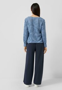Jasnoniebieska, teksturowana bluzka z wzorem liści, długimi rękawami i mankietami na guziki, zestawiona z ciemnogranatowymi spodnie o szerokich nogawkach oraz białymi trampkami.