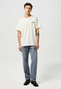 Biele tričko s krátkymi rukávmi a čiernym logom "Wrangler", skombinované so svetlomodrými rovnými džínsami a čiernymi členkovými čižmami.