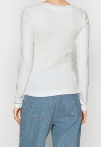 Vit långärmad topp med en åtsittande design och ribbad textur, kombinerad med lösa blå denimbyxor med två bakfickor.