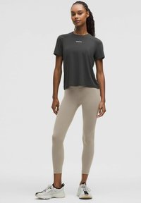 Grijze sport t-shirt met korte mouwen en het 'lululemon' logo, gecombineerd met beige hoge taille leggings en witte sneakers. Glad stoffen textuur.