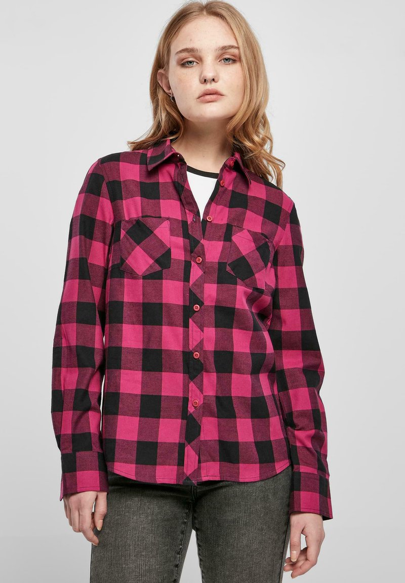 Chemise à carreaux avec de grands carrés roses et noirs, deux poches sur la poitrine, un col et un design à boutons. Le tissu a une texture douce.