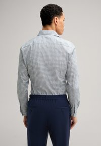 Camicia a maniche lunghe di colore azzurro chiaro con un motivo geometrico, caratterizzata da piccoli disegni. Abbinata a pantaloni con elastico in vita di colore blu navy scuro.