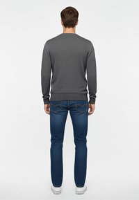Maglione grigio a maniche lunghe con texture, abbinato a jeans blu con un sottile motivo. Le sneakers bianche completano l'outfit.
