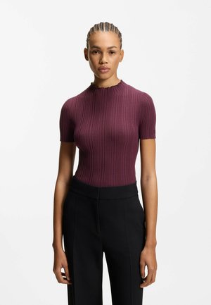 Bordeauxfarbenes, geripptes Kurzarmshirt mit hohem Halsausschnitt, kombiniert mit schwarzen Hosen mit weitem Bein und glatter Textur.