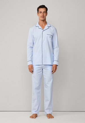 Conjunto de pijama a rayas azul claro hecho de algodón. Camisa de botones con un bolsillo y ribete negro; pantalones rectos a juego. Sin calzado.