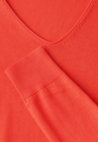 Korallefarbener Strickpullover mit V-Ausschnitt, gerippten Bündchen und glatter Textur. Nahaufnahme hebt die Farb- und Stoffkonsistenz hervor.