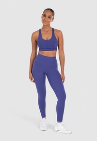 Sport-bh och leggings-set i djupt lila tyg, med en elegant design och mjuk yta, kombinerat med vita träningsskor.