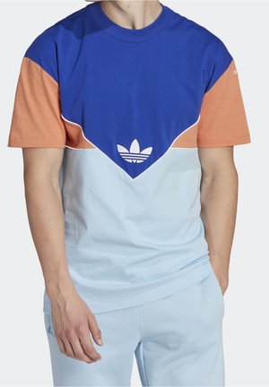 Homme portant un t-shirt bicolore avec des sections bleu, pêche et bleu clair, et un logo trefoil blanc d'Adidas sur la poitrine.