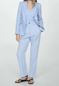 Costume bleu clair sur mesure comprenant un blazer ajusté avec des revers nets, un gilet assorti à boutons, et un pantalon droit.