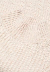 Pull rose pâle tricoté avec une texture côtelée et un col montant. Comprend des détails en tricot torsadé sur les épaules et un tissu lisse sur l'ensemble.