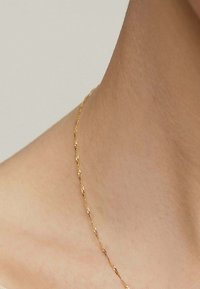 Collar de cadena de oro con un diseño trenzado, descansando sobre la piel. La cadena presenta una textura delicada con secciones alternas lisas y estriadas.