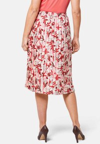 Gelaagde rok met een bloemenpatroon in rood, roze en beige tinten. Elastische tailleband en knielange ontwerp. Draagt met bruine hakken.