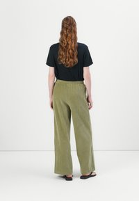 Olijfgroene corduroy broek met wijde pijpen van stevige stof; gecombineerd met een zwarte t-shirt met korte mouwen. Eenvoudige elastische tailleband.