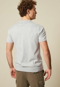 Lys grå kortærmet polo shirt med flad Krave og ribbet kant; glat tekstur og klassisk pasform, båret med olivengrønne bukser.