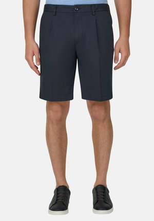 Czarne, sięgające do kolan, dopasowane spodenki męskie w połączeniu z czarnymi tenisówkami na neutralnym tle, stojące prosto.