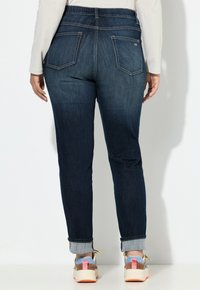 Tmavě modré džíny z denimu s tapered střihem, ohrnutými manžetami a dvěma zadními kapsami. Pas má jemnou elastickou gumu pro větší pohodlí.