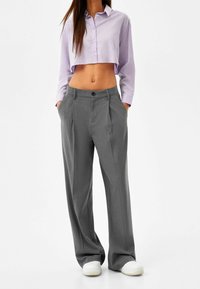 Cropped lavender shirt with long sleeves and buttons paired with gray high-waisted pleated trousers and white sneakers.