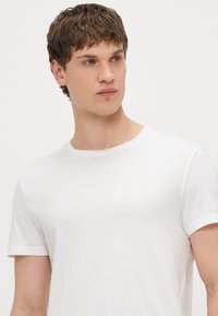 Fehér, rövid ujjú póló kerek nyakkivágással, könnyű anyagból készült, sima felületű és egyszerű kialakítású.